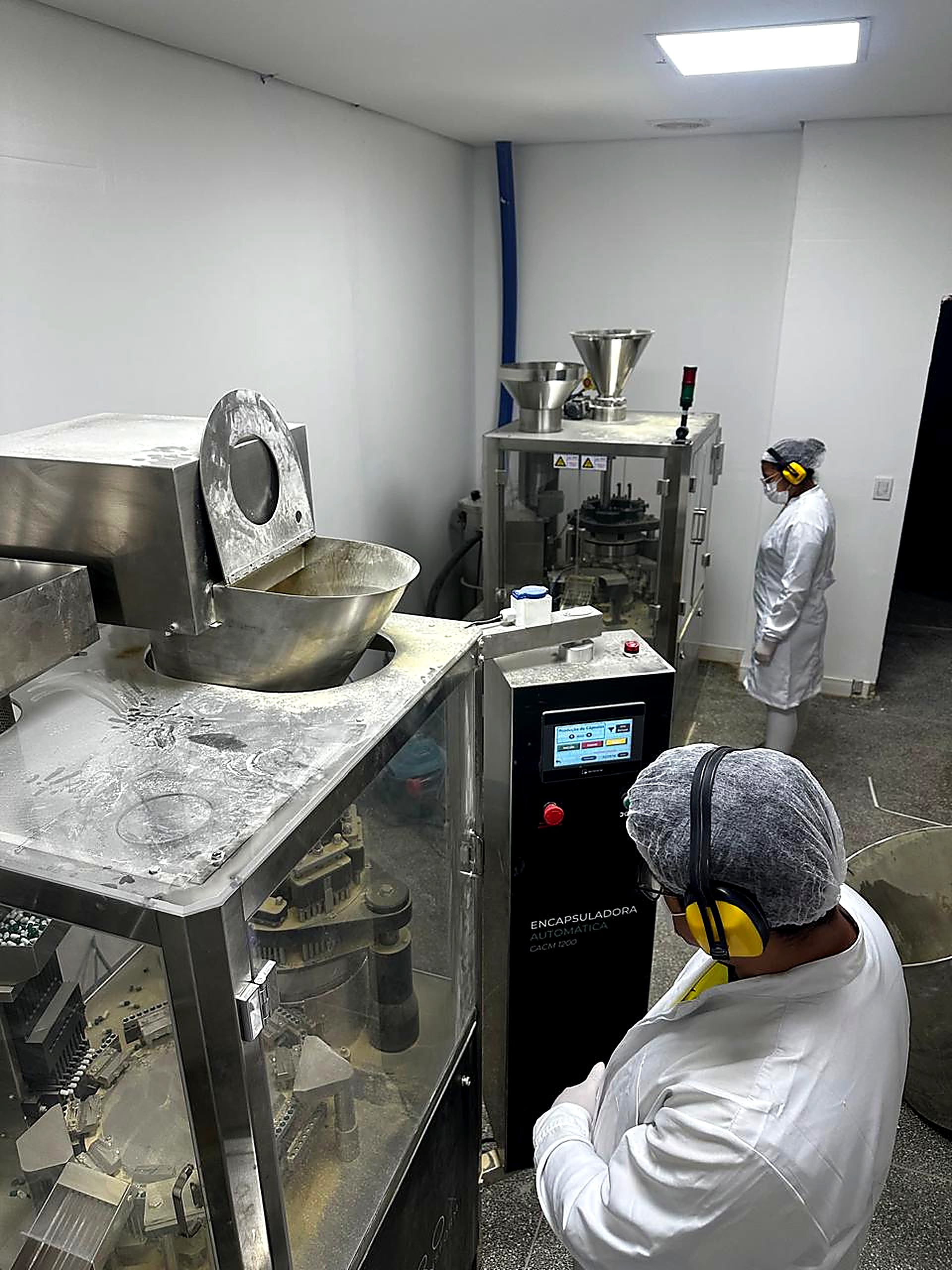 Linha de produção da fábrica MORBACH NUTRI: encapsuladora e máquina de envase com operadores